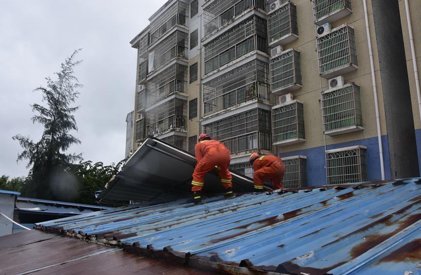 13日，定安县消防救援大队风雨中爬上屋顶处置一处被大风吹倒的铁皮。定安消防供图