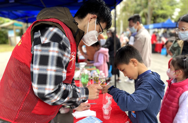 2023年世界湿地日主题游园宣传活动现场，志愿者与小朋友共同模拟湿地在自然中净化水质的过程。