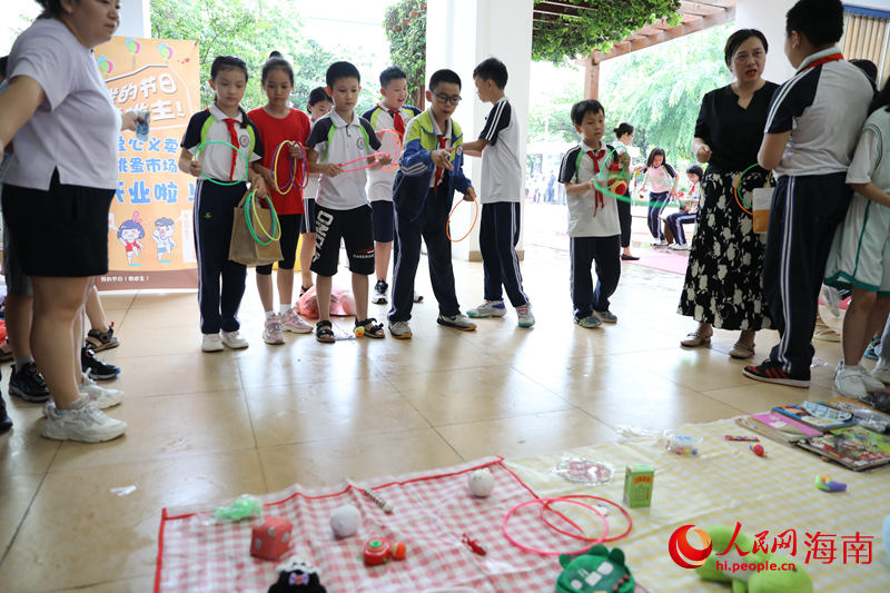 5月31日，在海口市第二十五小学公益跳蚤市场上，学生通过做游戏来赢得喜爱的物品。 人民网记者 孟凡盛摄